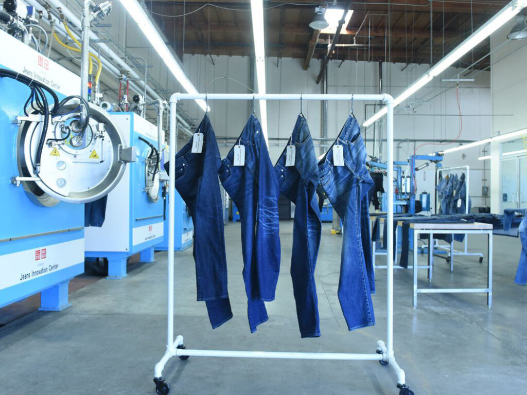 Industrial jeans innovation center with denim pants hanging on rack near advanced machinery.